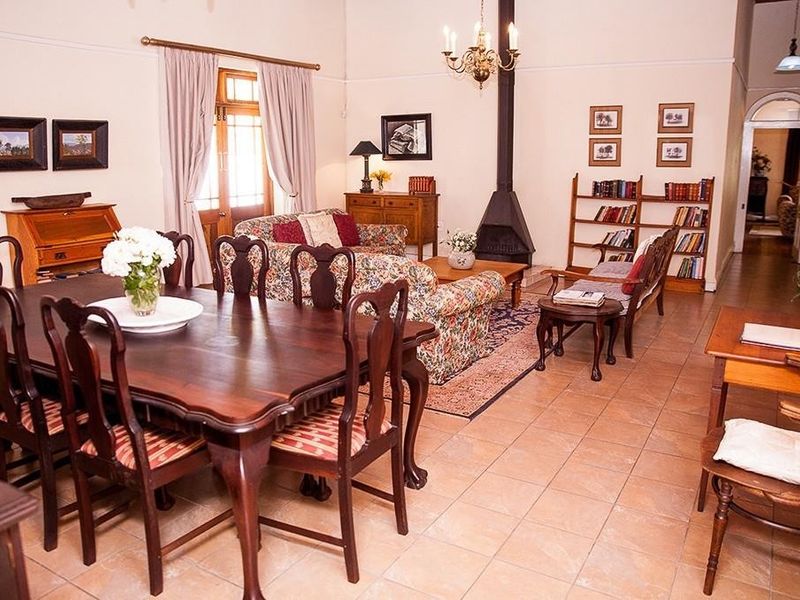 Spacious open-plan living and dining area featuring tiled flooring, a central freestanding fireplace, and a classic chandelier, leading into a hallway.