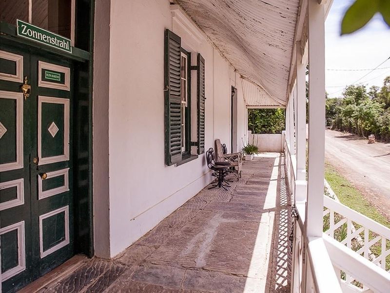 A charming covered veranda featuring traditional stone flooring, timber shutters, and a classic lattice balustrade overlooking the street.