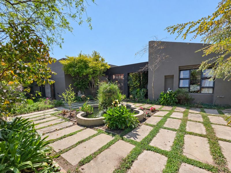 A well-maintained rear garden featuring concrete paving, a central water feature, and modern dark-toned exterior walls with aluminium window frames.