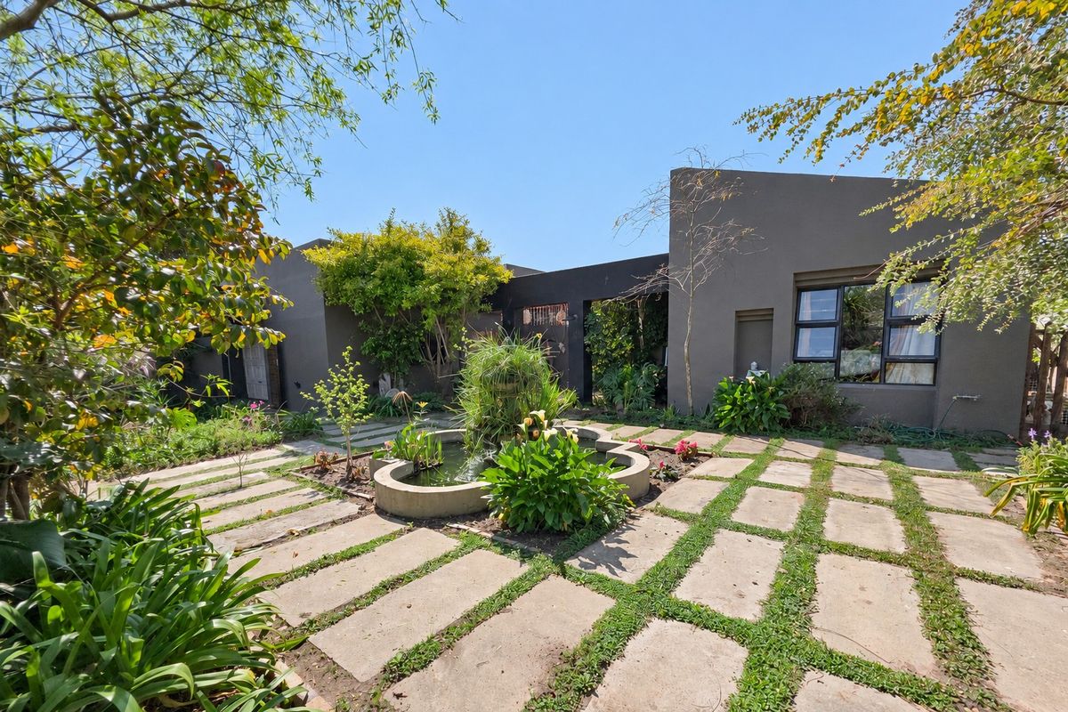 A well-maintained rear garden featuring concrete paving, a central water feature, and modern dark-toned exterior walls with aluminium window frames.