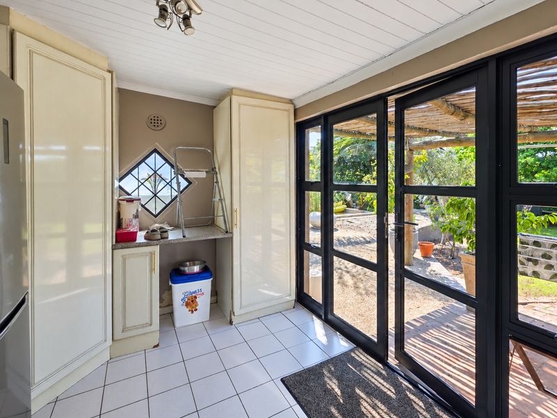A functional scullery area featuring built-in cabinetry, tiled floors, and large glass doors providing direct access to the outdoor garden space.