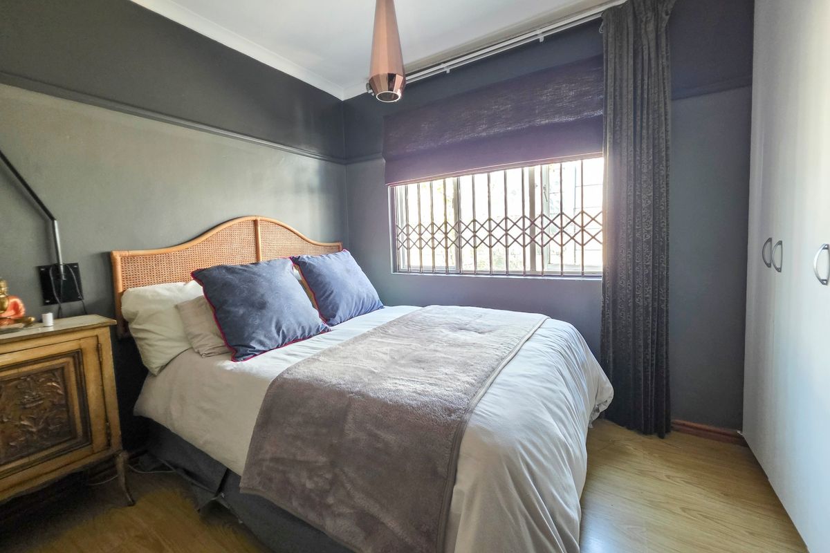 A well-maintained bedroom featuring laminate flooring, a built-in wardrobe, and a window fitted with a security gate.