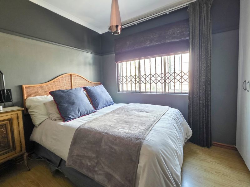 A well-maintained bedroom featuring laminate flooring, a built-in wardrobe, and a window fitted with a security gate.