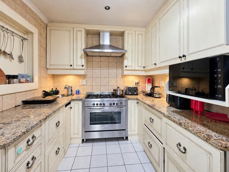 A well-maintained galley-style kitchen featuring granite countertops, stainless steel gas stove, extractor fan, and ample built-in cabinetry with a classic finish.