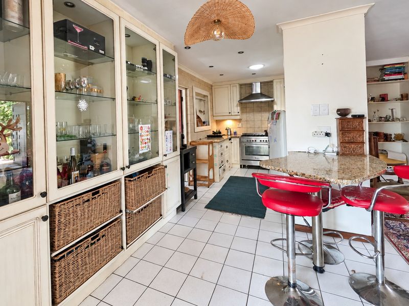 A functional kitchen featuring built-in cabinetry, granite breakfast bar, stainless steel gas stove, and tiled flooring with ample storage space.