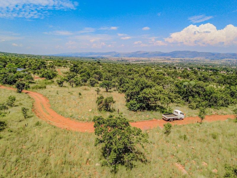An aerial view of a large, undeveloped residential plot featuring natural vegetation and a dirt access road with distant mountain views.