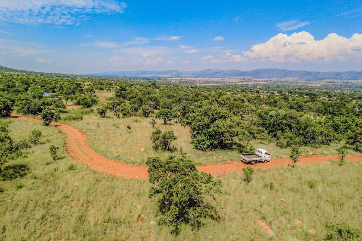 An aerial view of a large, undeveloped residential plot featuring natural vegetation and a dirt access road with distant mountain views.