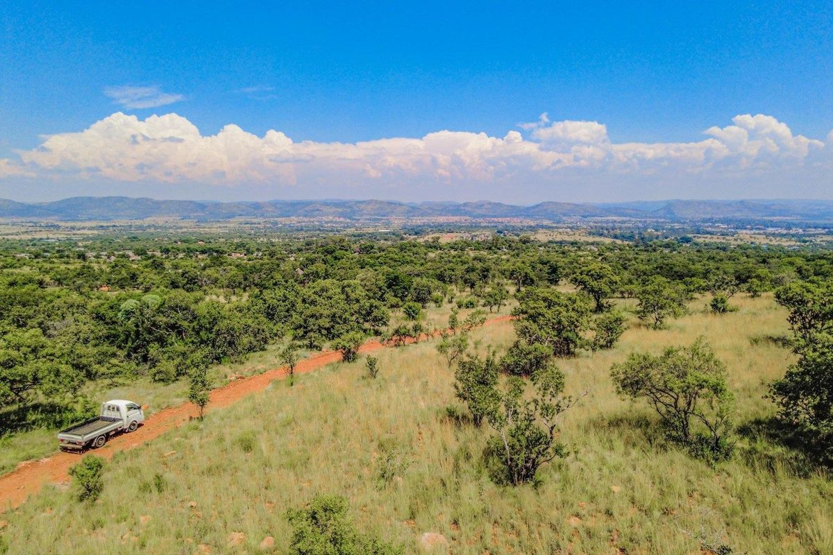 An aerial view of a large, undeveloped residential plot featuring natural vegetation and a dirt access road with distant mountain views.