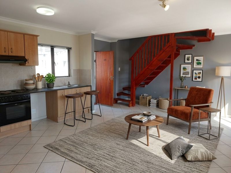 Open-plan living area featuring a functional kitchen with built-in cabinetry, tiled flooring, and a prominent wooden staircase leading to the upper level.