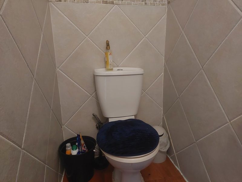 A compact bathroom featuring a standard toilet with a bidet spray and neutral diamond-patterned wall tiling.