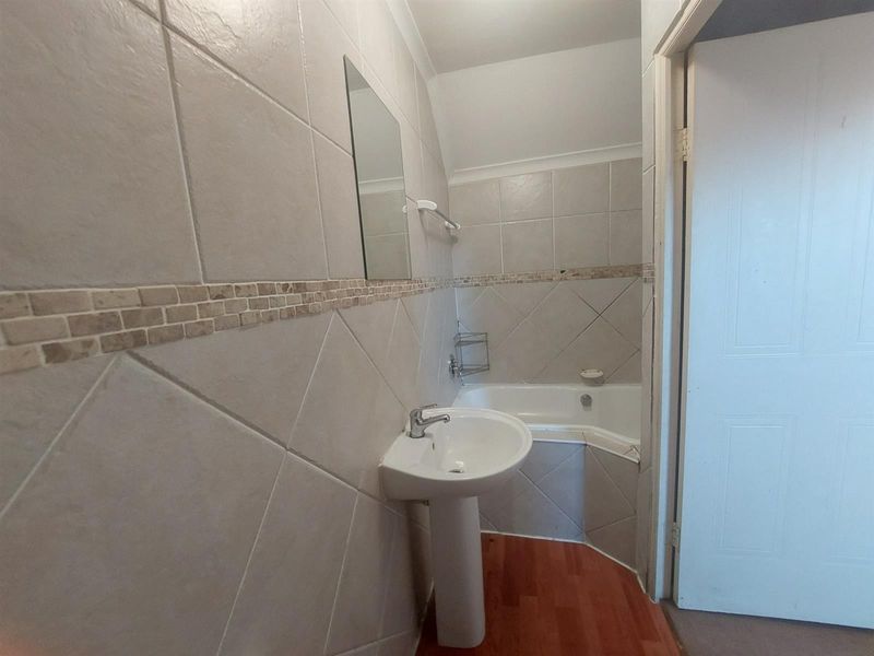 A functional bathroom featuring a pedestal basin, corner bathtub, and neutral wall tiling with a decorative mosaic border.