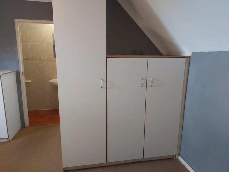 A bedroom featuring built-in cupboards under a sloped ceiling, with an adjacent view into a tiled bathroom.