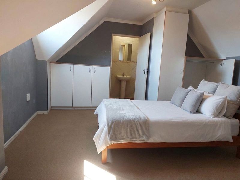 Attic-style bedroom featuring sloped ceilings, built-in storage cupboards, and direct access to an en-suite bathroom with a pedestal basin.