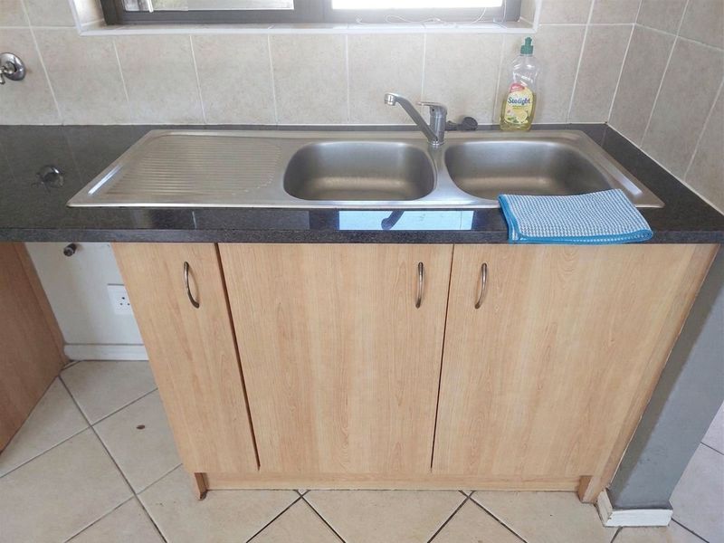 A functional kitchen area featuring a double bowl stainless steel sink, granite countertops, and light wood-finish cabinetry with tiled splashbacks.