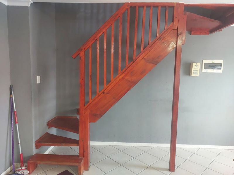 An interior view featuring a wooden staircase with a balustrade, tiled flooring, and an electrical distribution board mounted on a grey wall.