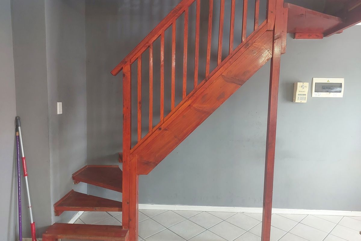 An interior view featuring a wooden staircase with a balustrade, tiled flooring, and an electrical distribution board mounted on a grey wall.