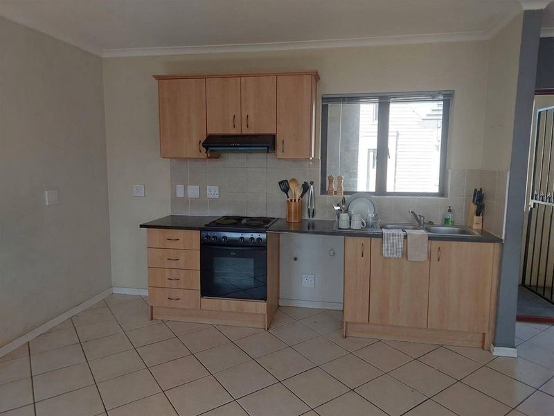 Functional kitchen featuring light wood-finish cabinetry, built-in oven and hob, tiled backsplash, and tiled flooring with a window for natural light.
