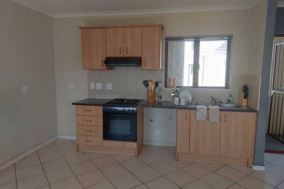 Functional kitchen featuring light wood-finish cabinetry, built-in oven and hob, tiled backsplash, and tiled flooring with a window for natural light.