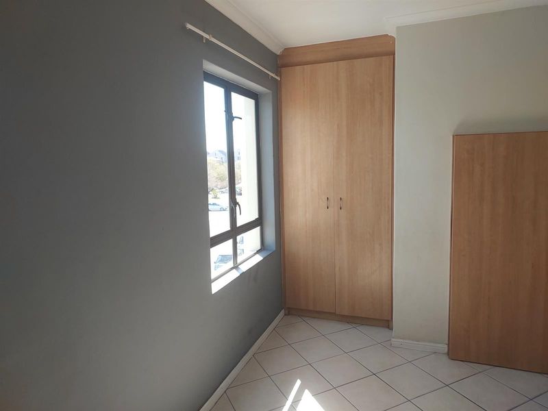 A bright, empty bedroom featuring tiled flooring, neutral wall tones, and built-in wooden cupboards providing ample storage space.