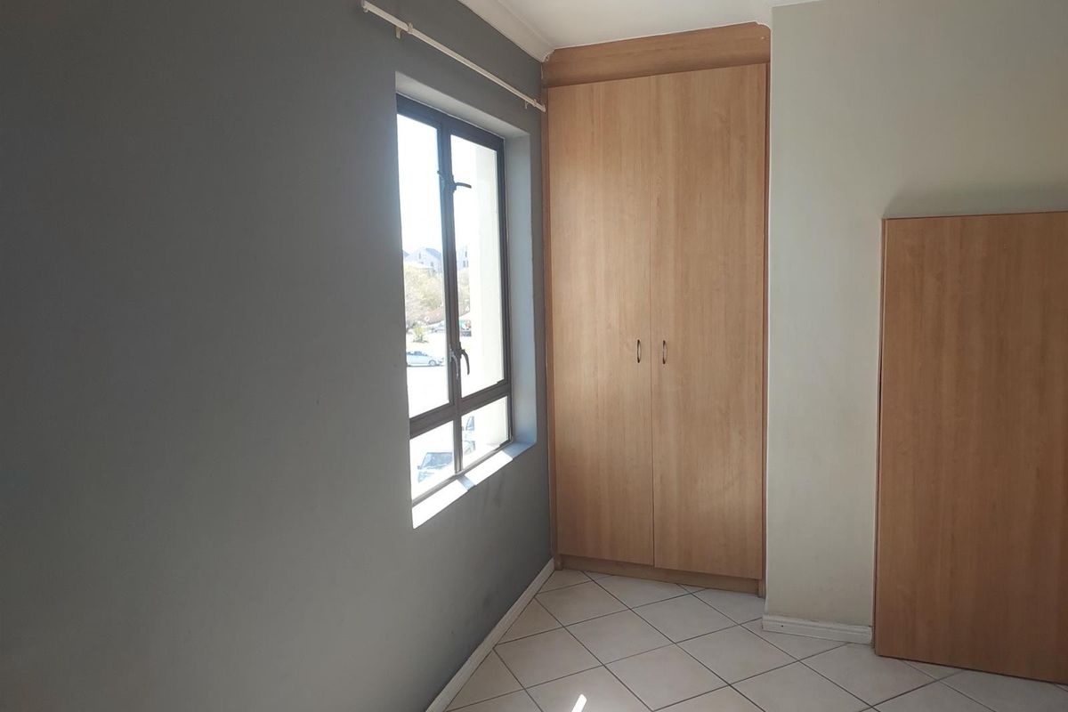 A bright, empty bedroom featuring tiled flooring, neutral wall tones, and built-in wooden cupboards providing ample storage space.