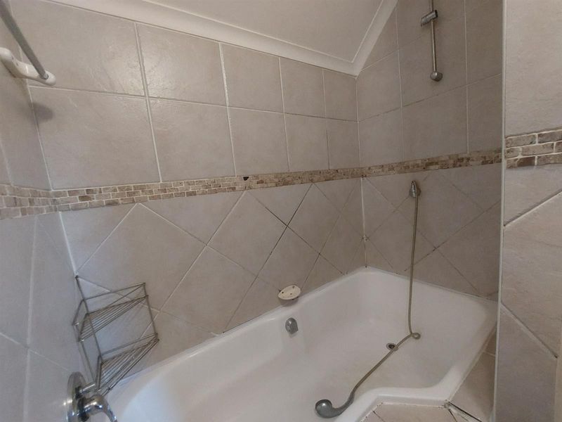 A bathroom featuring a built-in bathtub with a handheld shower attachment and neutral tiled walls with a decorative mosaic border.