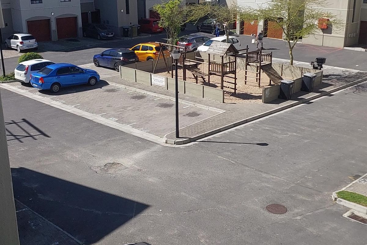 Elevated view of the apartment complex exterior, featuring a paved parking area and a communal children's play area.