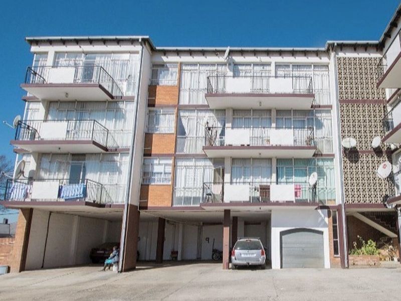 Front elevation of a multi-story apartment building featuring private balconies, a concrete driveway, and ground-level garage access.