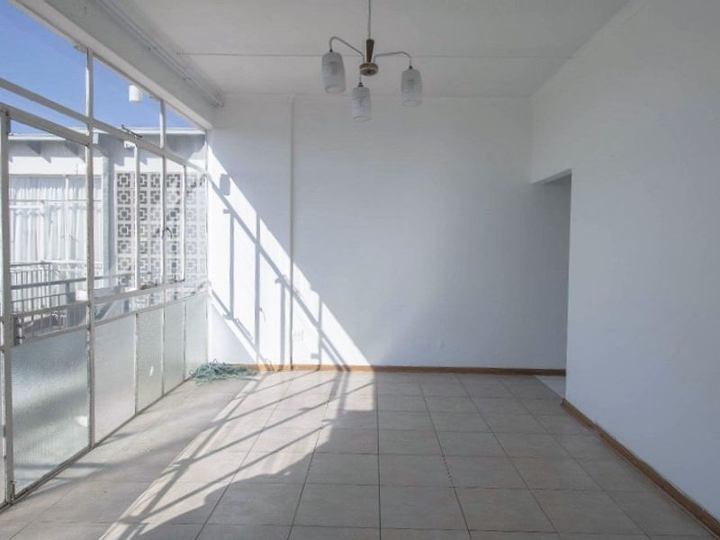 An empty, sunlit enclosed balcony featuring tiled flooring and large glass windows, offering a versatile space for a sunroom or relaxation area.