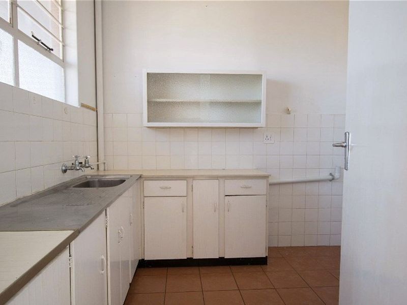 A functional scullery or laundry area featuring built-in cabinetry, a stainless steel sink, and tiled finishes, offering a blank canvas for renovation.