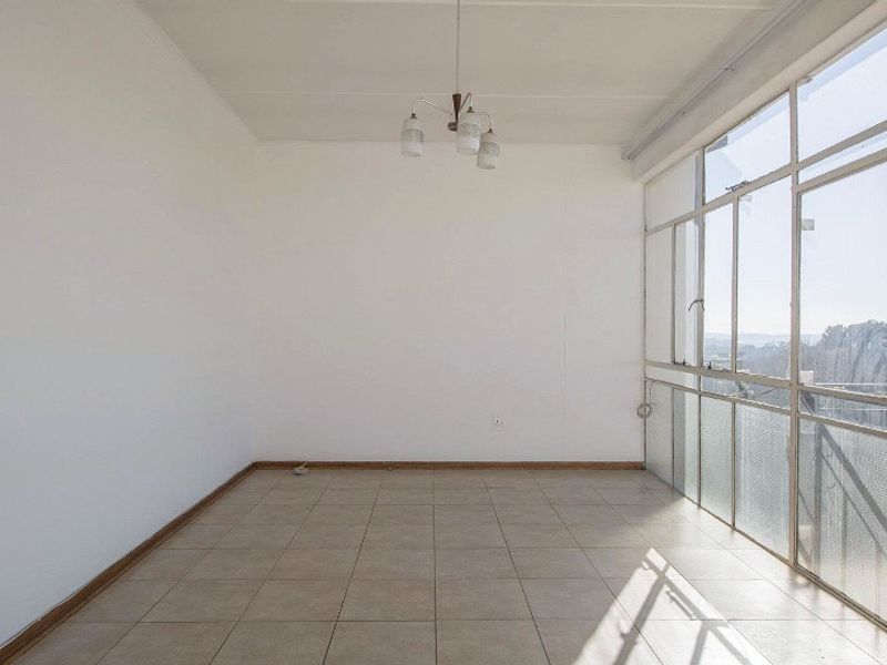 A bright, empty living area featuring tiled flooring and a large glass wall providing natural light and exterior views.
