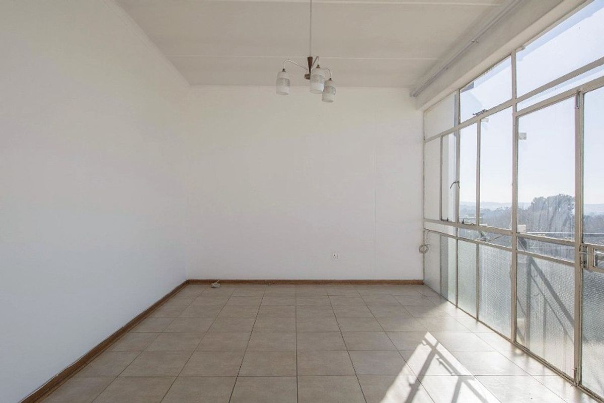 A bright, empty living area featuring tiled flooring and a large glass wall providing natural light and exterior views.