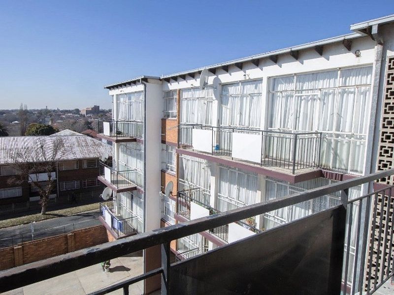 Exterior view of an apartment building featuring multiple levels with private balconies, metal railings, and large glass sliding doors.