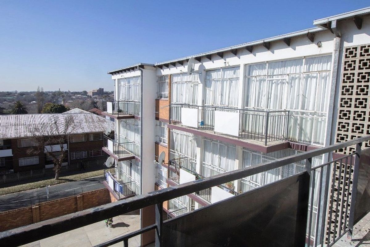 Exterior view of an apartment building featuring multiple levels with private balconies, metal railings, and large glass sliding doors.