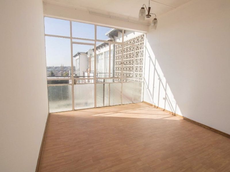 An empty living room featuring large glass windows, laminate flooring, and a ceiling light fixture, offering a bright and open space.