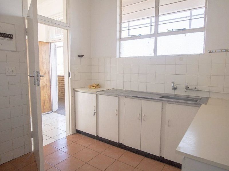 A functional, empty kitchen featuring built-in white cabinetry, a stainless steel sink, tiled backsplash, and tiled flooring, offering potential for modernization.