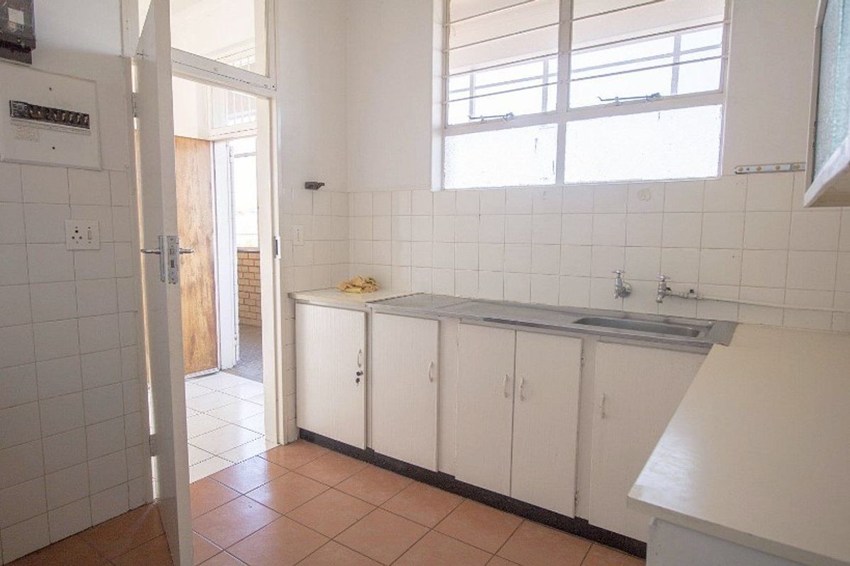 A functional, empty kitchen featuring built-in white cabinetry, a stainless steel sink, tiled backsplash, and tiled flooring, offering potential for modernization.