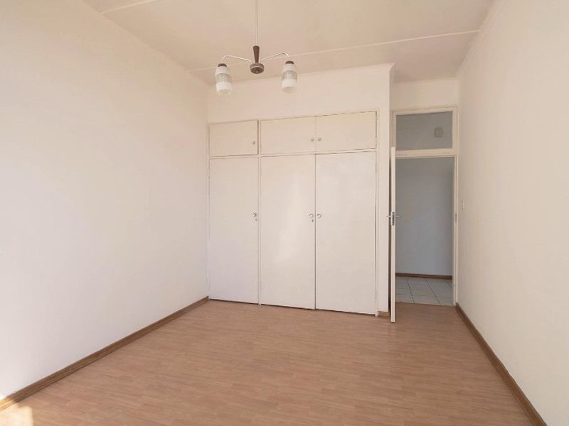 A clean, empty bedroom featuring light-toned laminate flooring and ample built-in cupboard storage space.