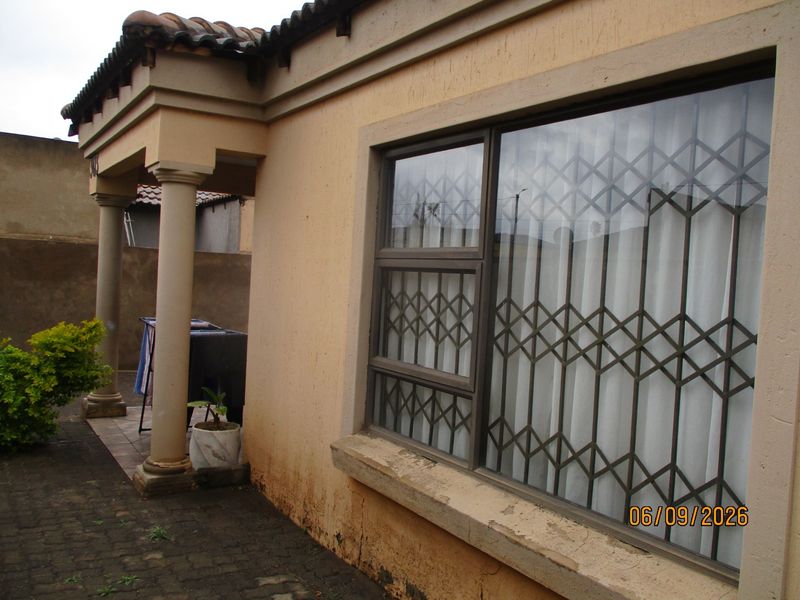 Front exterior view of the house featuring concrete columns, security gates on windows, and a paved walkway with visible exterior wall maintenance required.