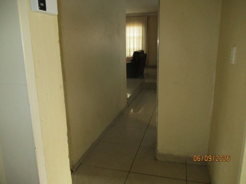A narrow interior hallway featuring tiled flooring and an installed alarm system keypad, leading towards an adjacent living area.