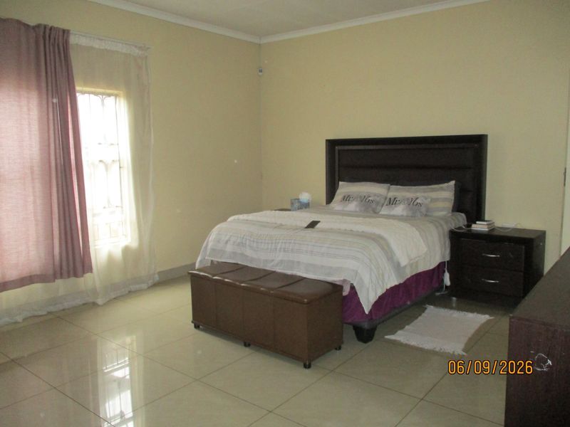 A spacious bedroom featuring tiled flooring, neutral wall tones, and a window fitted with security bars.