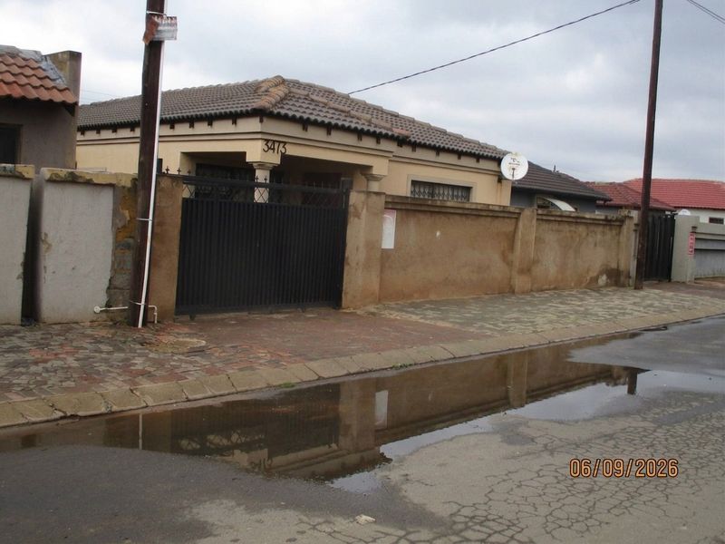 Front exterior view of a single-story house featuring a tiled roof, perimeter wall, and metal driveway gate.