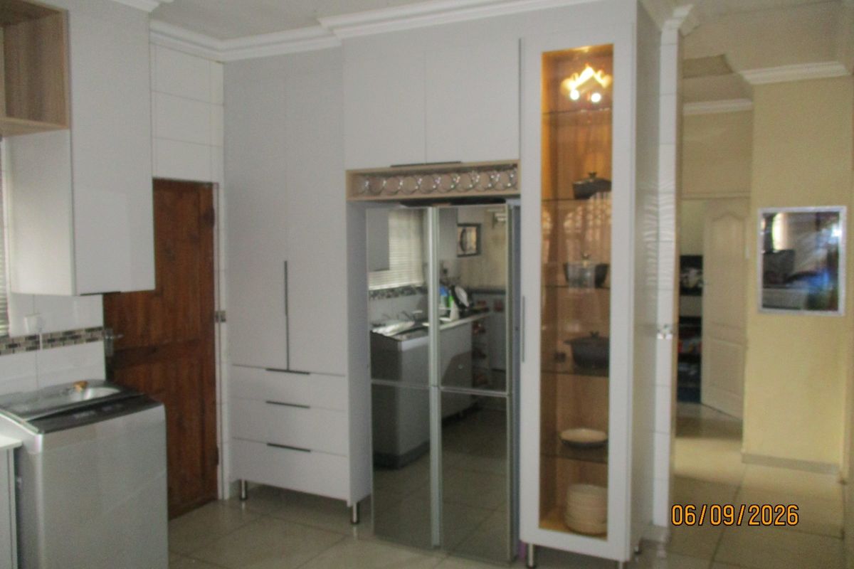 A well-maintained kitchen area featuring modern white built-in cabinetry, a glass display unit, and tiled flooring with crown molding details.