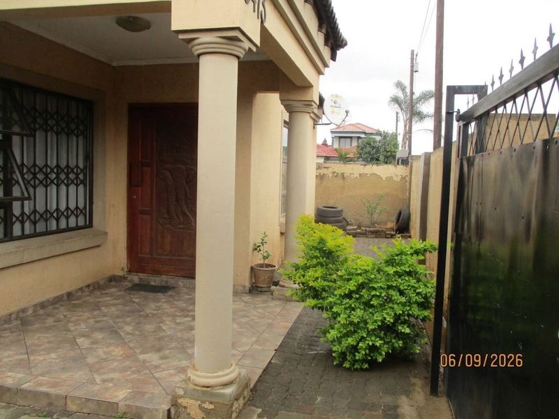 Front entrance area featuring a tiled porch with decorative columns, a solid wood door, and a gated boundary wall.