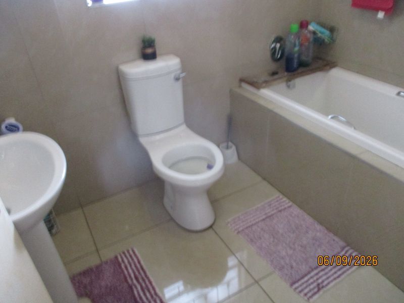 A functional bathroom featuring a pedestal basin, a standard toilet, and a built-in bathtub with tiled walls and flooring.