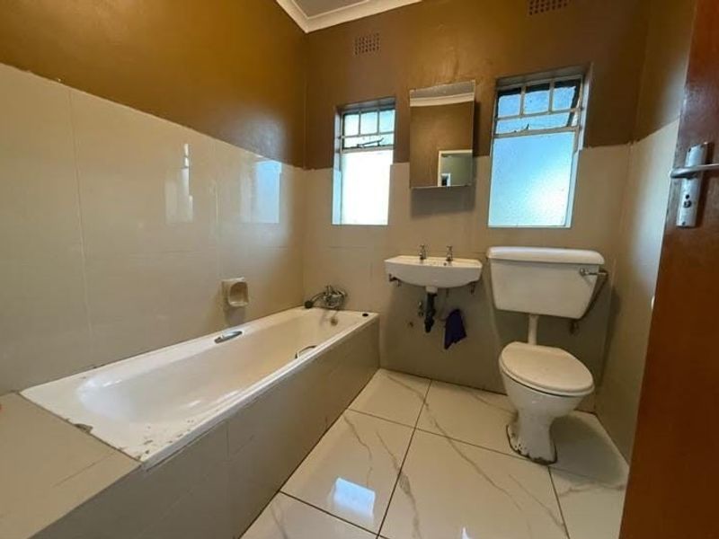 A functional bathroom featuring a bathtub, wall-mounted basin, and toilet with tiled finishes, requiring minor cosmetic updates to refresh the space.