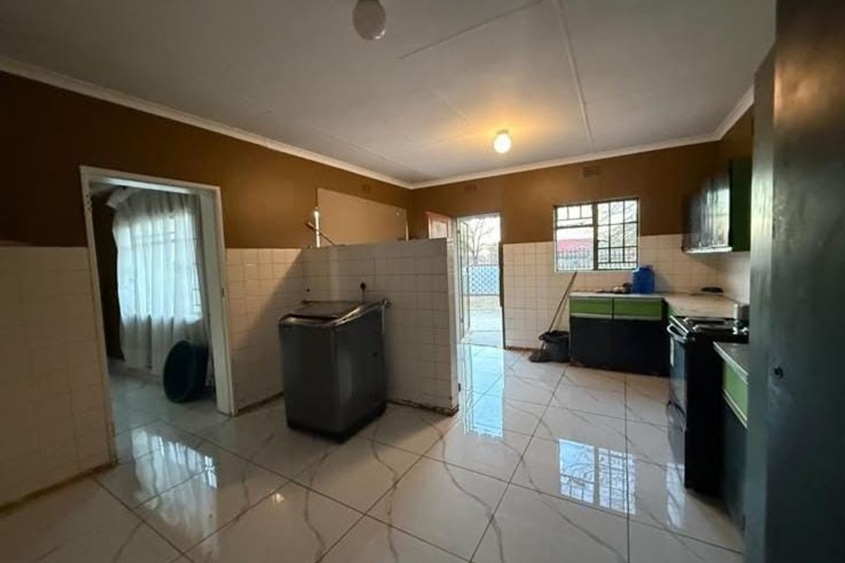A functional kitchen space featuring tiled flooring, built-in cabinetry, and a tiled splashback, currently requiring some finishing touches to complete the aesthetic.