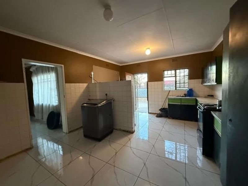 A functional kitchen space featuring tiled flooring, built-in cabinetry, and a tiled splashback, currently requiring some finishing touches to complete the aesthetic.