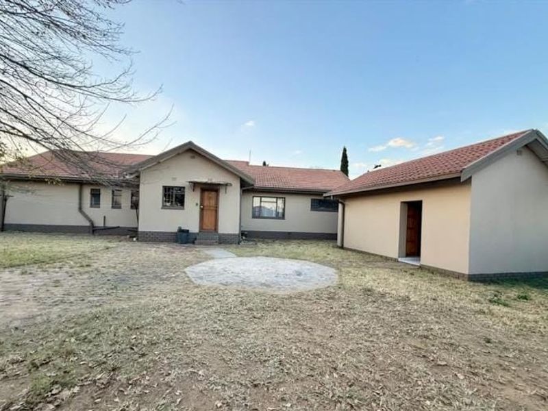 Rear view of the house featuring a detached garage, tiled roof, and a paved outdoor area set within a spacious garden.