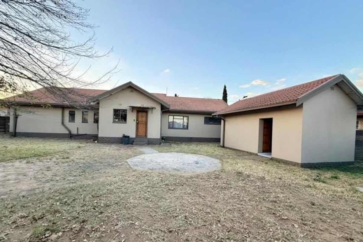 Rear view of the house featuring a detached garage, tiled roof, and a paved outdoor area set within a spacious garden.