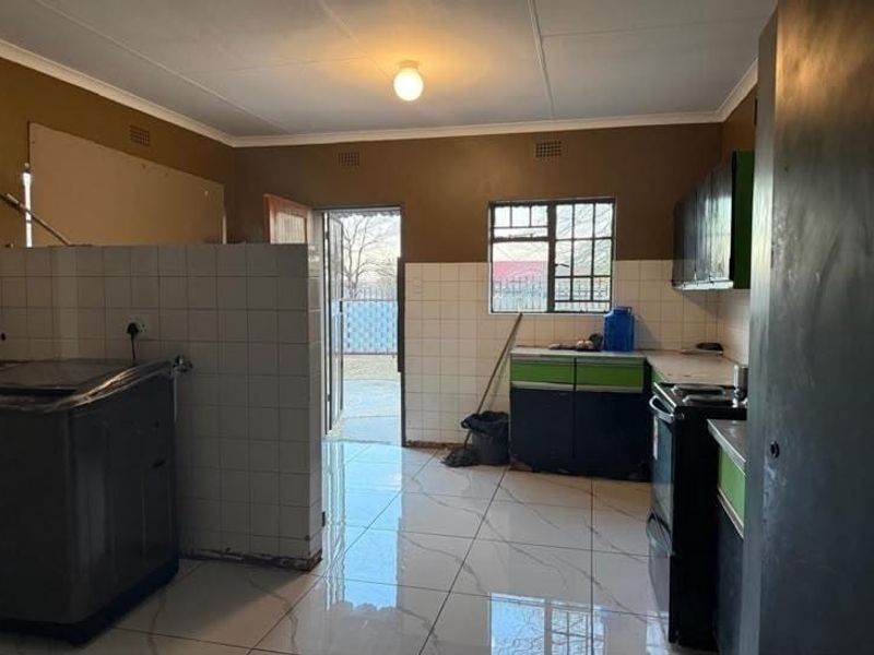 A functional kitchen area featuring tiled flooring, tiled splashbacks, and built-in cabinetry with direct access to the exterior.